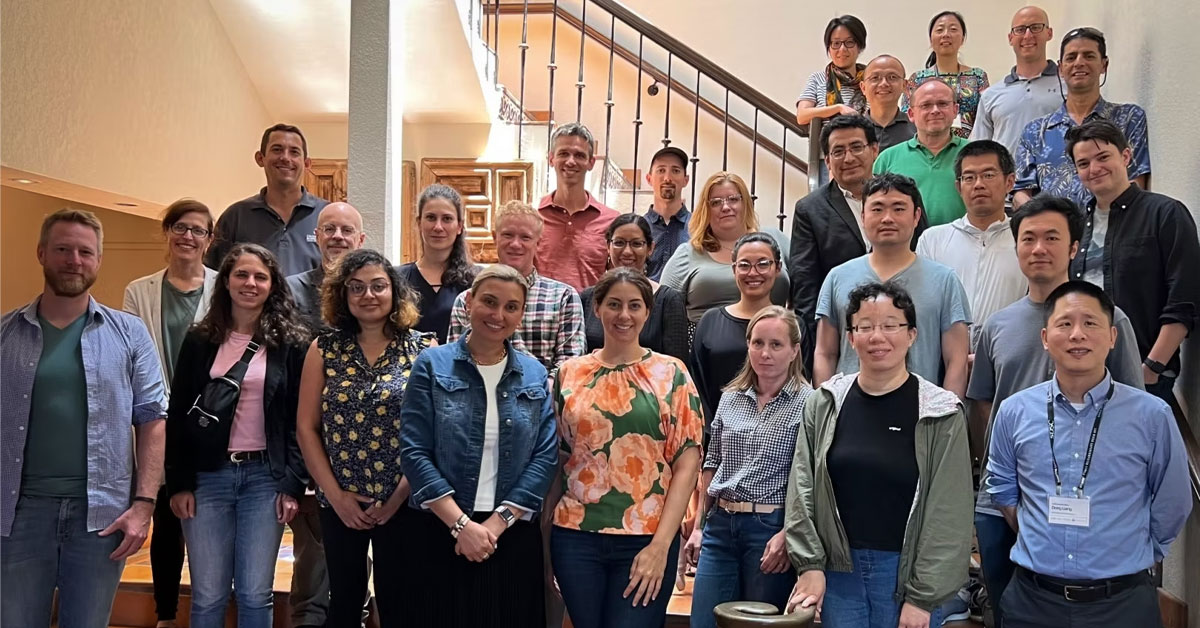 A large, diverse group of researchers and professionals pose for a group photo on an indoor staircase.
