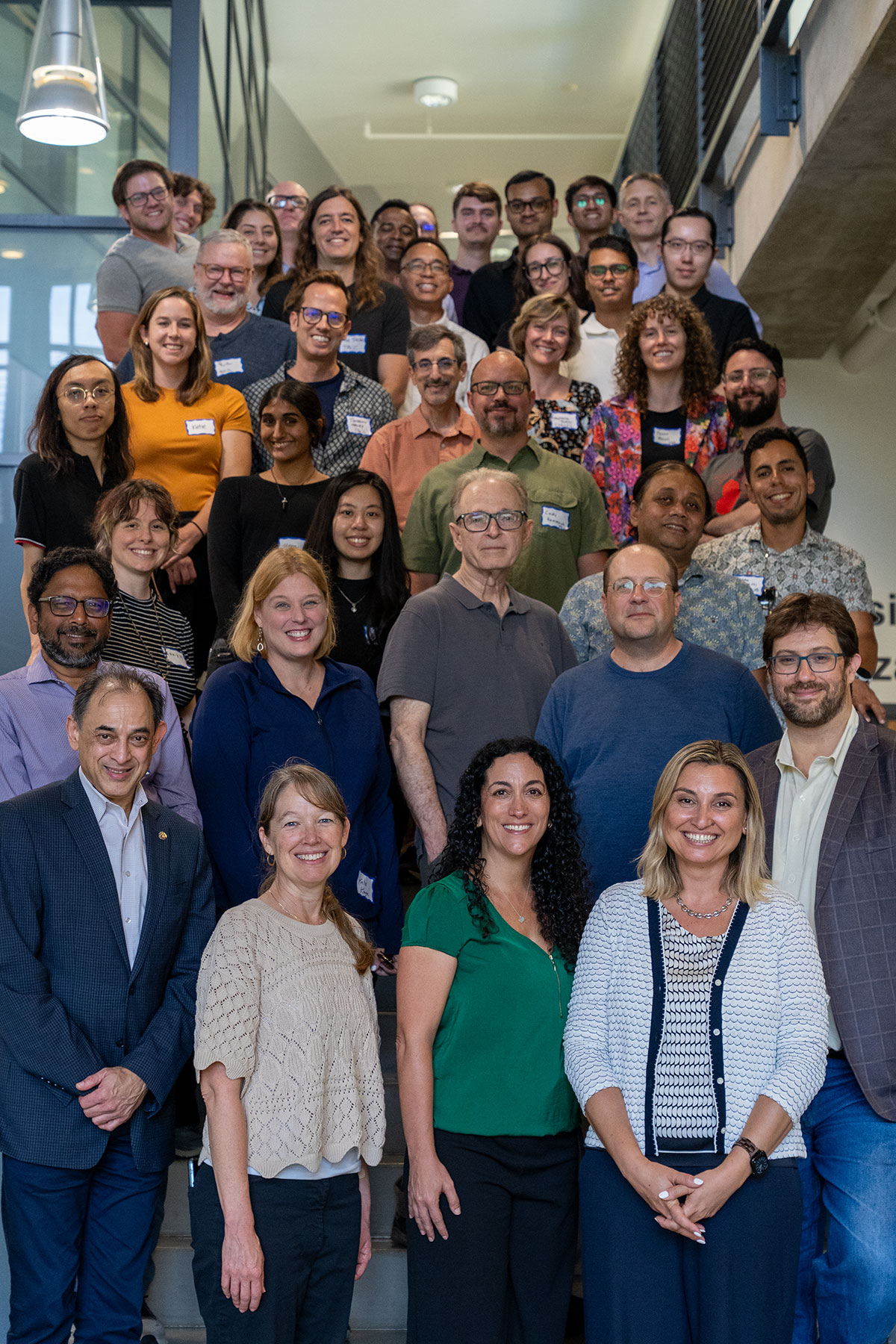 A group of workshop attendees and researchers poses for a group photo on an indoor staircase.