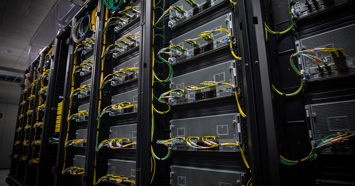 Server racks with interconnected yellow and green cabling in a dark data center cluster.